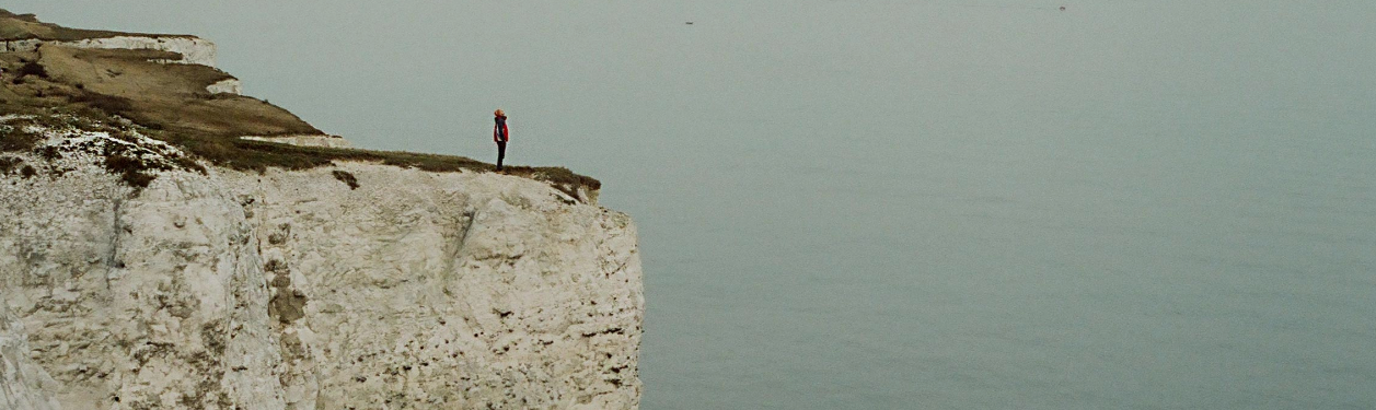 Image of a person standing on the edge of a cliff overlooking the ocean